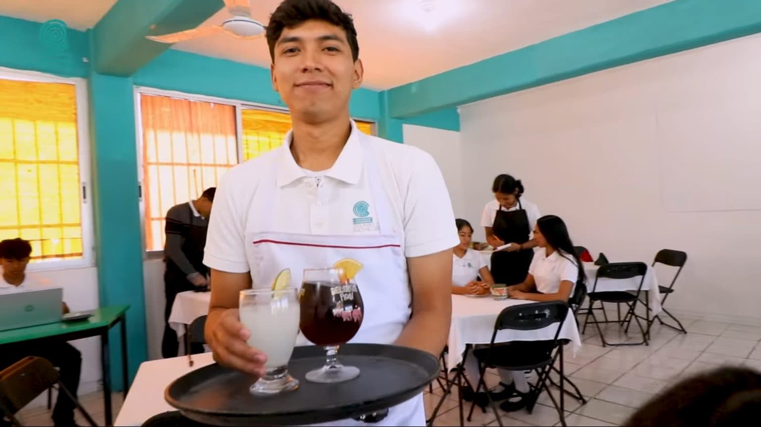 Estudiante sirviendo bebidas en una charola durante una práctica de servicio