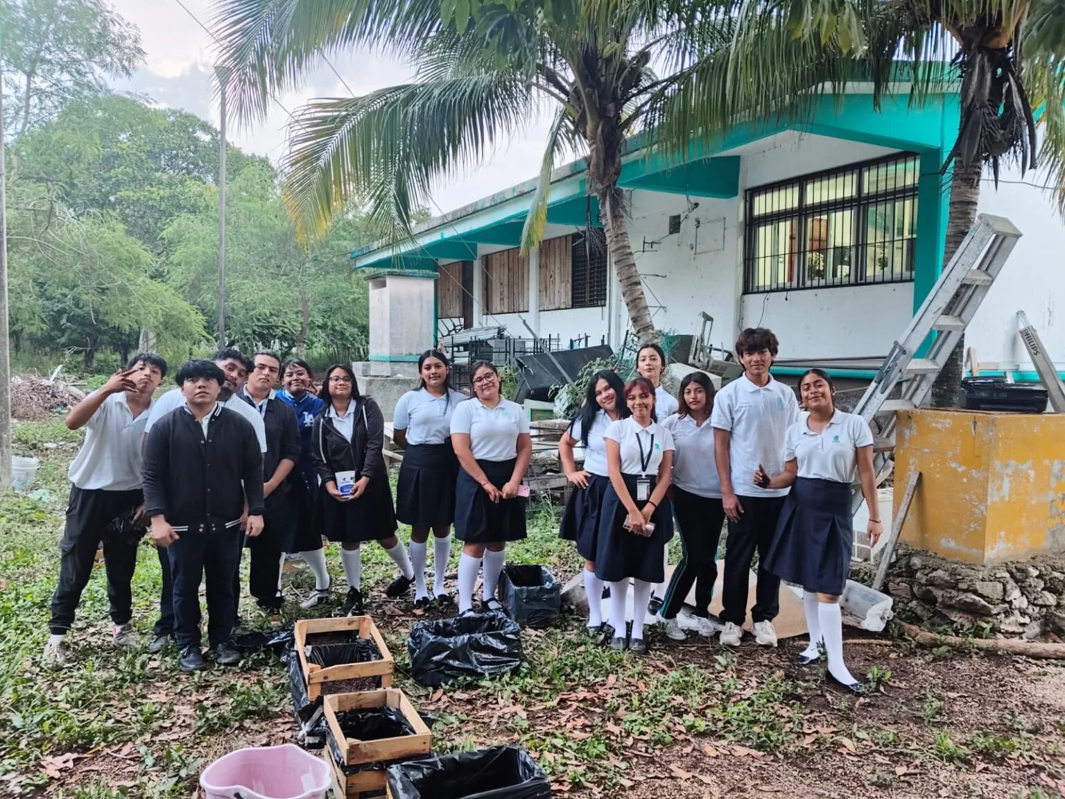 Estudiantes junto a cajones de siembra del huerto escolar en un área verde del plantel.